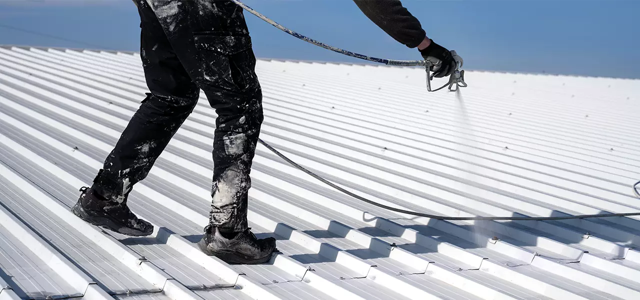 Handwerker tr&auml;gt die Aqua Thermo Dachfarbe im Airless-Verfahren auf ein helles Trapezblechdach auf